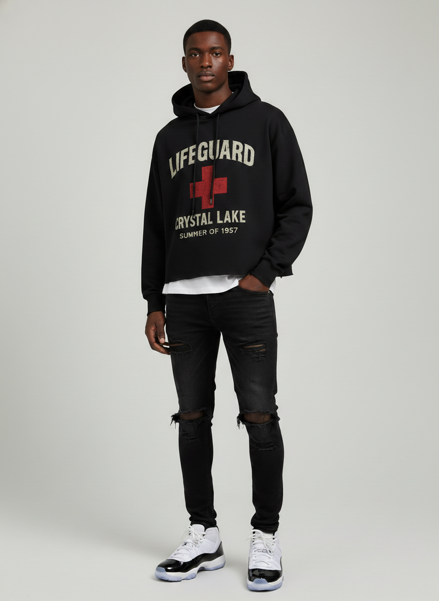 Model wearing the Screaming Saints Crystal Lake Lifeguard Summer of 1957 cropped black horror hoodie with a distressed red cross graphic.